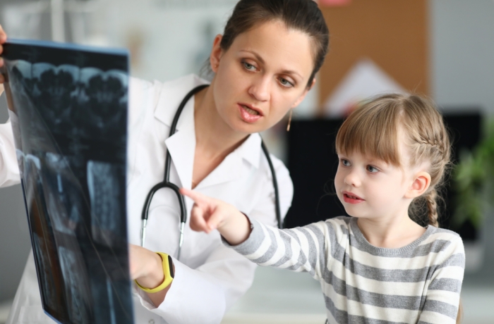 Portrait of experienced focused pediatrician showing skiagram of serious sick child. Little girl pointing on x-ray by finger. 